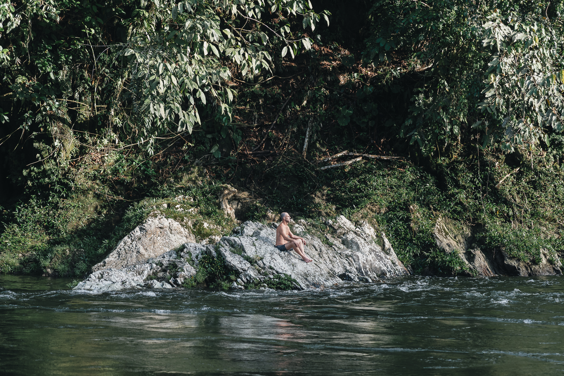 Visitante sentado en una roca en medio del río